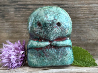 A kodama nature spirit ceramic guardian statue glazed in a turquoise and copper glaze. It has a wide face, two big eyes, and cute little arms.