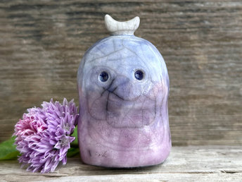 A kodama nature and forest spirit kami ceramic raku sculpture glazed in a bottom-to-top gradient of soft purple to blue. It has a gentle face, and a white crescent moon on its head.
