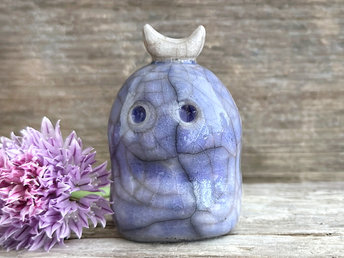 A kodama nature and forest spirit kami ceramic raku sculpture glazed in blue. It has a gentle face, and a white crescent moon on its head.