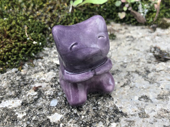 Raku ceramic sculpture of a sweet little sitting bear, like a teddy bear. He has a lovely, friendly face, cute little arms, and he's glazed in soft purple and mauve.