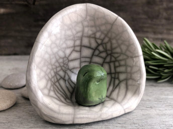 A Shinto kodama nature spirit kami of forests and trees in his own little kamidana shine. The kodama is very sweet and glazed in green. The shrine is white with beautiful raku patterns and vaguely egg-shaped.