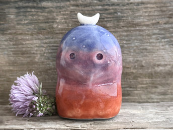 A kodama nature and forest spirit kami ceramic raku sculpture glazed in a bottom-to-top gradient of burnt red-orange to mauve to purple to indigo. It has a gentle face, some small white marks like stars on its head, and a white crescent moon on top.