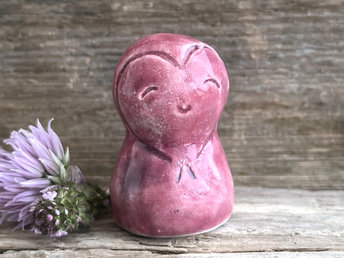 A smiley and loving Jizo Shinto raku ceramic sculpture talisman glazed in warm, pinky red colour with hints of purple. She has a heart shape carved around her kind, gentle face and is a wonderful smooth shape to hold in the hand.