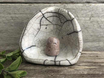A sweet Shinto Jizo statue in his own little shine. The Jizo looks very happy and loving and is glazed in pale and slightly stronger peach-pink. The shrine is white and vaguely egg-shaped. Both Jizo and shrine are raku stoneware.