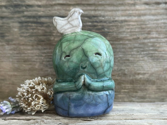 a shinto jizo nature spirit guardian raku ceramic sculpture glazed in a bottom-to-top gradient of blue to forest green to spring green. they have a happy, smiley face, little praying hands, and a sweet white bird on their head.