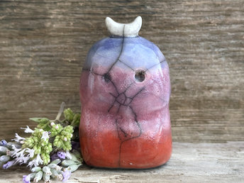 A kodama nature and forest spirit kodama kami ceramic raku sculpture glazed in a bottom-to-top gradient of red-orange to mauve to blue. It has a gentle face, and a white crescent moon on its head.