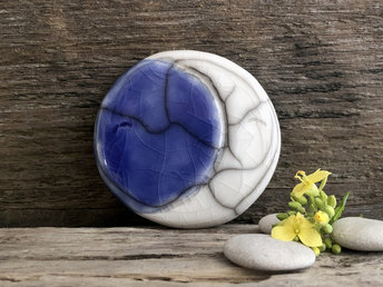 Flat, round raku ceramic sculpture of a moon. On the left side is a white crescent, and the rest of the circle is blue to make a complete moon. It has a sweet face and is a very gentle statue for Shinto, shamanism, or pagan worhsip.