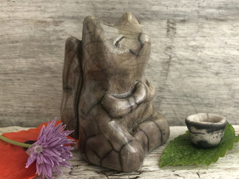 Raku ceramic sculpture of a fox sitting in a meditation position. He is glazed in a soft grey-brown colour and he has little praying hands (paws). His face is very kind and gentle.