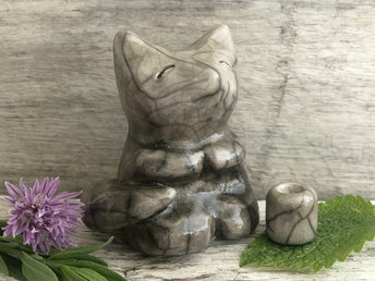 Raku ceramic sculpture of a fox sitting in a meditation position. She is glazed in soft greys and browns, and she has little praying hands (paws). Her face is very kind and gentle.