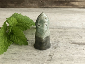 Little ceramic sculpture of an earth, stone, and tree elemental glazed in green and brown. He looks maybe a little like a leaf combined with a standing stone and has a gentle face.