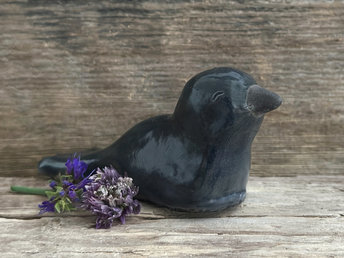Raku ceramic sculpture of a sitting raven. It is glazed in dark blue-grey, and its beak is left natural, unglazed black.