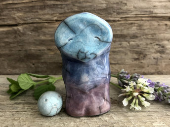 Raku ceramic sculpture of a tall turquoise-blue, violet, and purple spirit with a calm face. Next to him is a small round spirit glazed in pale turquoise. 
