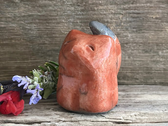 Raku ceramic sitting kitsune fox spirit sculpture glazed in a deep red-orange colour. It has a sweet, gentle face, and its tail points up its back.