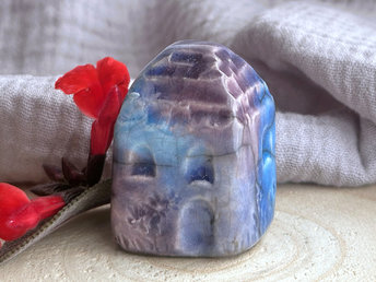Tiny raku ceramic cottage glazed in turquoise, blue, indigo, and violet-purple. Its roof is carved to look like slates. It has a carved door and windows and lots of plant and flower carvings too.