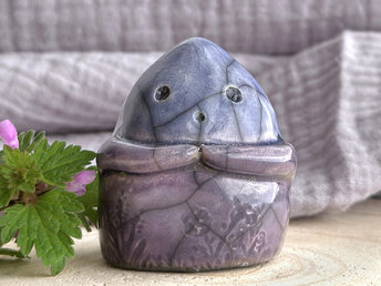 a vaguely dome-shaped nature spirit ceramic sculpture. it is glazed in a bottom-to-top gradient of violet to blue and has plant and flower carvings on its body. it also has a gentle face, and two little arms across its front.