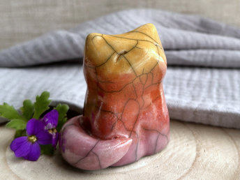 Raku ceramic sitting fox glazed in a gradient from mauve to orange to golden yellow (bottom to top). It has a kind face, and its tail is curled around its body.