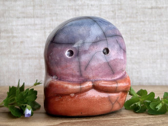 A kodama nature spirit ceramic guardian statue glazed in a top-to-bottom gradient of blue to violet to mauve to red-orange. It has a wide face, two big eyes, and cute little arms.