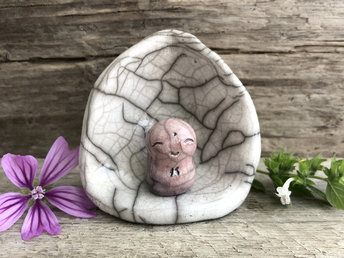 A sweet Shinto Jizo statue in his own little shine. The Jizo looks very happy and loving and is glazed in warm, pale reddish pink with hints of blue violet. The shrine is white and vaguely egg-shaped. Both Jizo and shrine are raku stoneware.