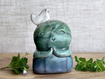 a shinto jizo nature spirit guardian raku ceramic sculpture glazed in a bottom-to-top gradient of blue to forest green to spring green. they have a happy, smiley face, little praying hands, and a sweet white bird on their head.