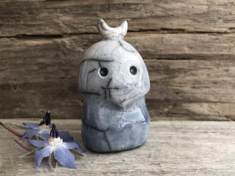A kodama nature and forest spirit kami ceramic raku sculpture glazed in soft blue and white with a gentle face and a crescent moon on its head.