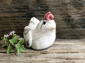 Raku ceramic chicken sculpture. She is glazed in white with an orange beak and a bordeaux-red chicken thingy on her head.
