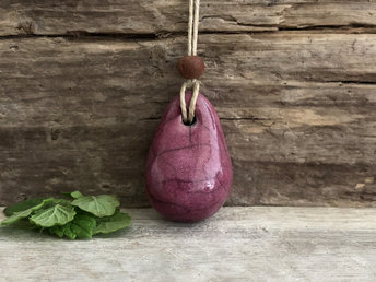Raku ceramic worry pendant shaped a little like a bendy pear and glazed in a deep Bordeaux red-pink. It has a sandalwood bead above it and is strung on a flax cord.