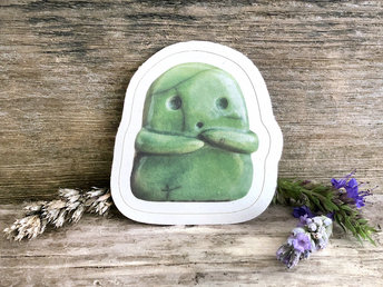 a sticker of a green ceramic kodama kami nature and tree spirit guardian. it has an sweet ooooo face and two little arms, and it's very cute! there is a thin white border all around the image.