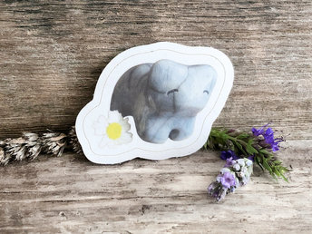 a sticker of a pale blue raku cermic bear sculpture. it has a sweet, friendly face, and there is a daisy next to it (part of the sticker). there is a thin white border around the image of bear and daisy.