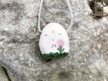 Ceramic Shinto Jizo pendant glazed in white with a green and pink spring flower design, a yellow sun, and a sweet smiling face.