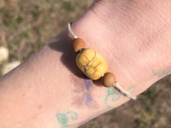 Yellow raku ceramic cylindrical Shinto Jizo bead bracelet with two ethical sandalwood beads. It is strung on an adjustable eco-hemp cord. Jizo looks very happy and sunny!