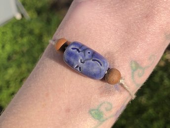 Blue raku ceramic cylindrical Shinto Jizo bead bracelet with two ethical sandalwood beads. It is strung on an adjustable eco-hemp cord. Jizo looks very happy and kind!