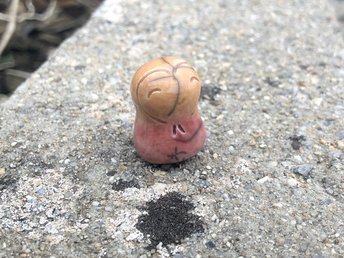 A smiley, loving, happy little Jizo Shinto raku ceramic sculpture talisman in shades of soft red and orange with a little heart around her face.