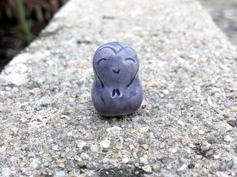 A smiley, loving, and very happy Jizo Shinto raku ceramic sculpture talisman in shades of blue and violet with a heart around her sweet face.