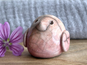 small and round raku ceramic bird sculpture glazed in a top-to-bottom gradient of pale peach to pale pinky red. it has a kind, gentle, and mildly intense face.