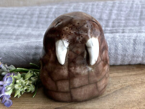 a brown stubby walrus raku sculpture with two white tusks. he has a happy face and smiling eyes.