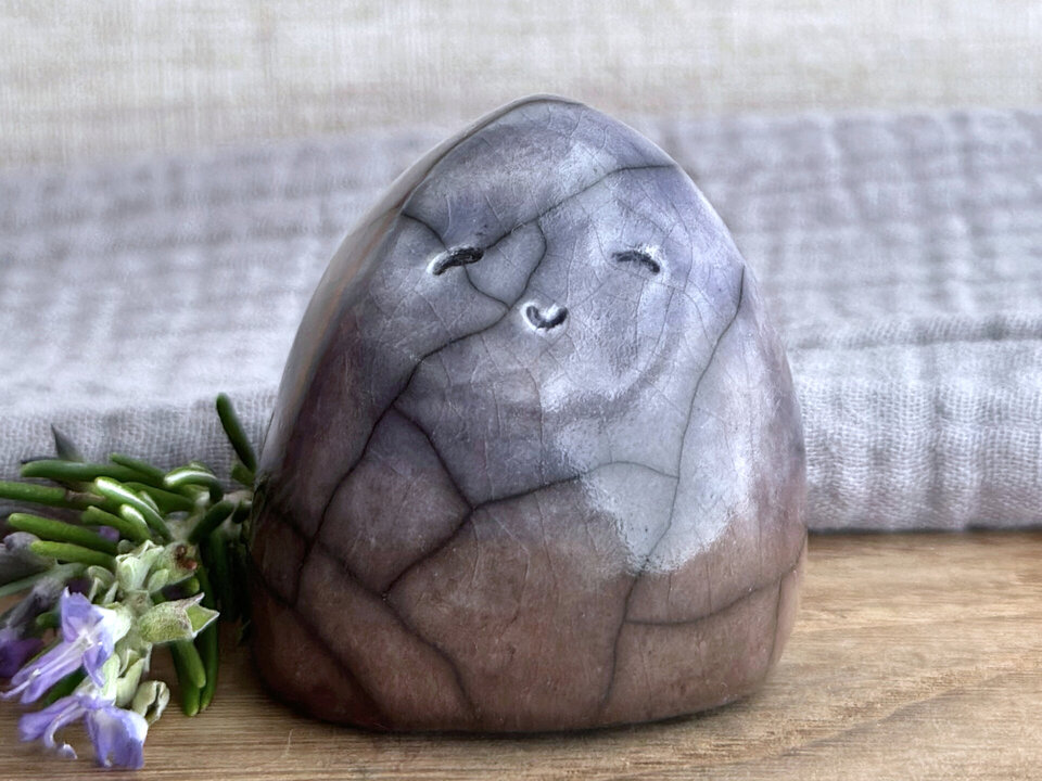 raku ceramic gnome spirit glazed in a bottom-to-top gradient of soft brown to pale indigo violet. it has a gentle, kind face.