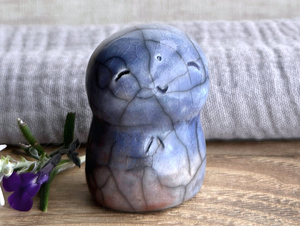 a smiley and loving Jizo Shinto raku ceramic sculpture talisman glazed in blue with hints of a pale. soft rust colour in places. they have a kind, gentle face and are a wonderful smooth shape to hold in the hand.